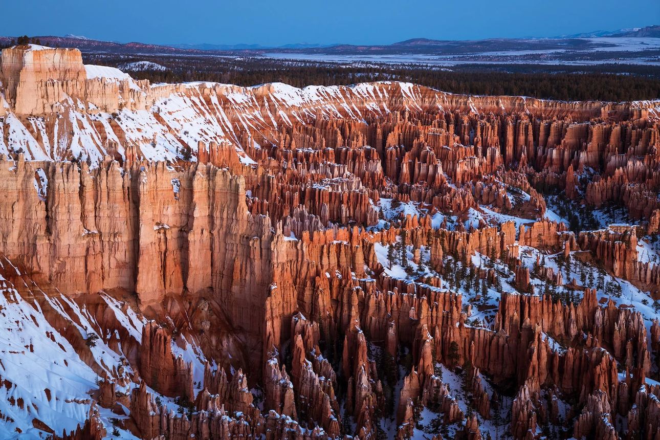 Fine art landscape photograph of Bryce Canyon's snow-dusted hoodoos glowing in warm sunrise light beneath a deep blue winter sky, Utah.