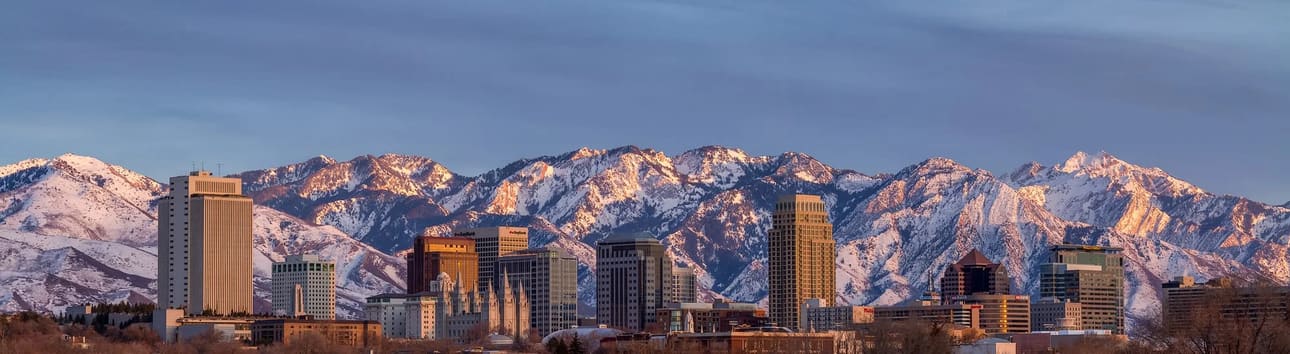 Panoramic view of the Salt Lake City skyline at sunset with the Wasatch Mountains covered in snow and glowing in golden light