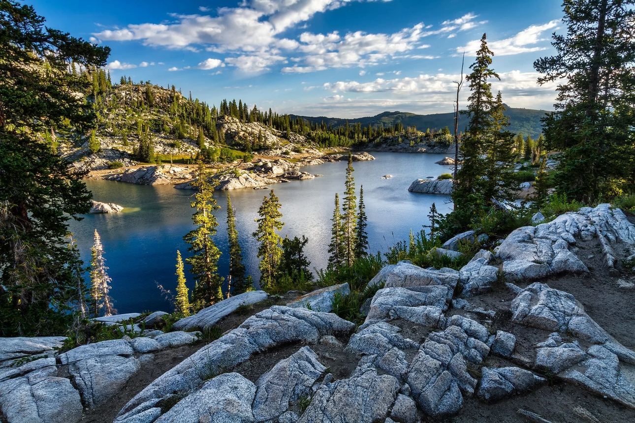 Lake Mary, an alpine lake surrounded by granite cliffs and pine trees in the Wasatch Mountains during golden hour with reflections on calm water.