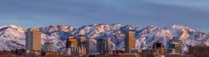Panoramic view of the Salt Lake City skyline at sunset with the Wasatch Mountains covered in snow and glowing in golden light